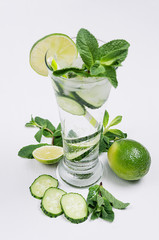 Fototapeta premium Fresh summer organic drink with slices cucumber, ice, lime, mint and ingredients on white wood table, closeup.