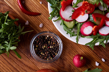 Creative fresh vegetable salad with ruccola, cucumber, tomatoes and raddish on white plate, selective focus