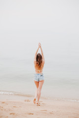 back view of girl stretching on sandy beach and looking at ocean
