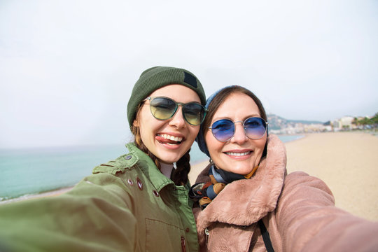 Mother and adult daughter are doing selfie on the beach going crazy and showing tongueSunset light.Happy and positive emotions.Hipster family.Parents and teenagers.Summer vacation self-portrait