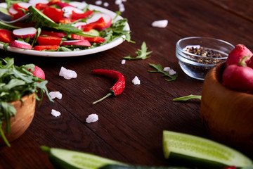 Creative fresh vegetable salad with ruccola, cucumber, tomatoes and raddish on white plate, selective focus