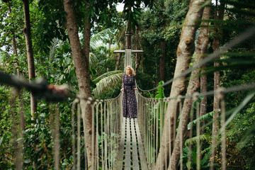 Serious woman in dress standing on footbridge in jungle