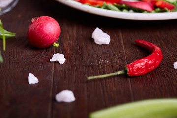 Fresh red radish in wooden bowl among plates with vegetables, herbs and spicies, top view, selective focus.