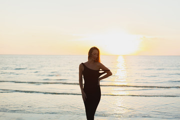 attractive woman posing in dress near ocean during sunset