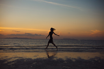 silhouette of woman running on ocean beach during sunset