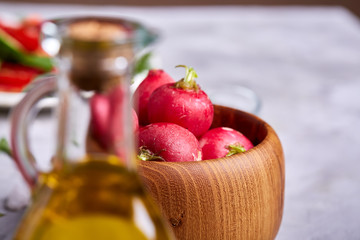 Fresh red radish in wooden bowl among plates with vegetables, herbs and spicies, top view, selective focus.