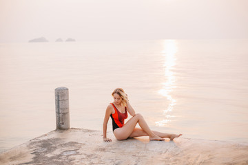 Fototapeta na wymiar beautiful girl sitting on pier in swimsuit near ocean