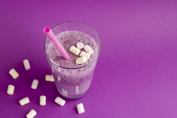 Glass of berry smoothie and marshmallow with straw on purple background. Pink milkshake with copy space. Healthy drink. Blueberry cocktail.