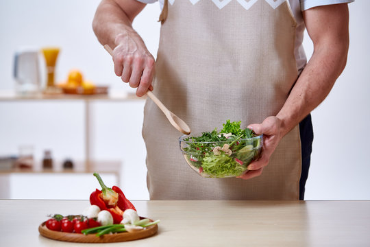 Man cooking at kitchen making healthy vegetable salad, close-up, selective focus.