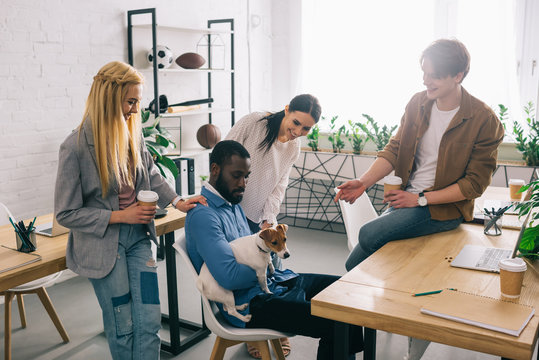 African American Businessman Sitting With Dog Surrounded By Smiling Colleagues