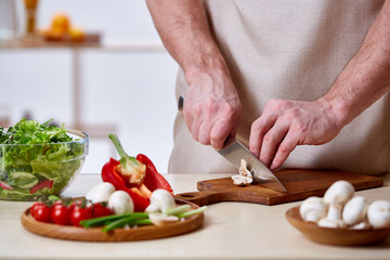 Man cooking at kitchen making healthy vegetable salad, close-up, selective focus.