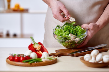 Man cooking at kitchen making healthy vegetable salad, close-up, selective focus.