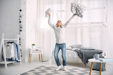 Excellent news. Merry afro american boy jumping while throwing up pillows