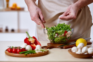 Man cooking at kitchen making healthy vegetable salad, close-up, selective focus.