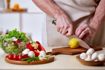 Man cooking at kitchen making healthy vegetable salad, close-up, selective focus.