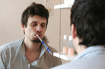 Tortured sleepy only waking man in front of the mirror with a toothbrush in his mouth.
