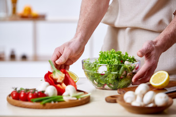 Man cooking at kitchen making healthy vegetable salad, close-up, selective focus.