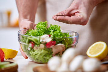 Man cooking at kitchen making healthy vegetable salad, close-up, selective focus.