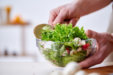 Man cooking at kitchen making healthy vegetable salad, close-up, selective focus.