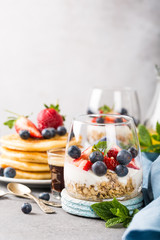 Oatmeal granola with berries and yogurt and panccakes on light gray concrete background. Healthy breakfast food concept with copy space.
