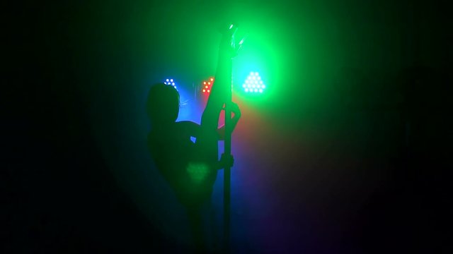 A flexible sexy girl in striped stripes is dancing a sensual dance on a pole in the dark under the lights of multi-colored searchlights. Pole dance. Slow motion.