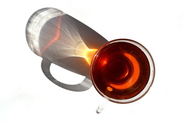 Hot black tea in transparent glass cup with long rainbow shadow in shaft of sunlight. Isolated....