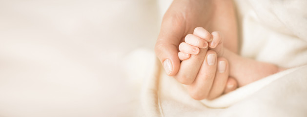 Female hand holding her newborn baby's hand. Mom with her child. Maternity, family, birth concept. Copy space for your text. Banner - 200852490