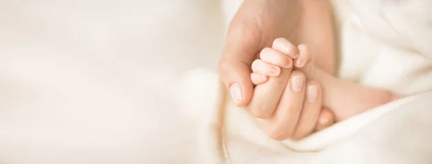 Fototapeten Female hand holding her newborn baby's hand. Mom with her child. Maternity, family, birth concept. Copy space for your text. Banner © jchizhe