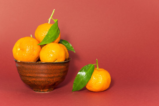 Still life studio shot of a red ceramic bowl with black texture filled with fresh orange tangerines on red background.