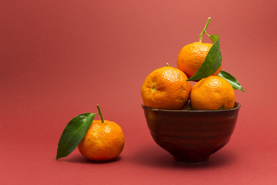 Still life studio shot of a red ceramic bowl with black texture filled with fresh orange tangerines on red background.