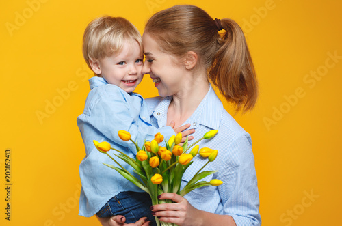 concept of mother's day. mom and baby son with flower on colored background.