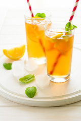 Glasses of iced tea with lemon slices and mint on white wooden background