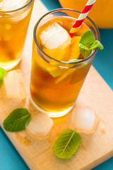 Glasses of iced tea with lemon slices and mint on turquoise wooden background