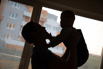 Silhouette of baby boy with Down syndrome and his dad opposite the window