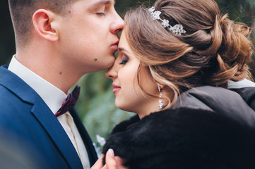 A gentle kiss of the newlyweds. Winter wedding. Close-up portrait of young bride and groom.