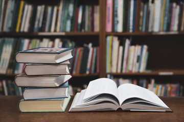Open book on wood desk in the library room, Book stack in the library room and blurred bookshelf for business and education background, Back to school concept