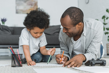 african american father drawing with son on floor at home