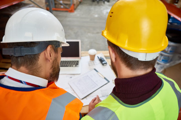 High angle of two unrecognizable construction workers looking at blueprints and floor plans on site