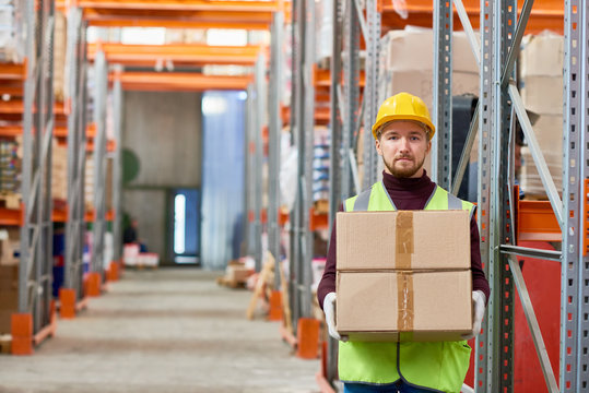 Portrait of young  warehouse worker holding cardboard box and looking at camera while doing shipping and deliveries, copy space