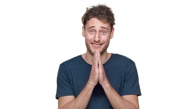 Portrait of nervous european guy in t-shirt posing with praying hands and worrying with fright or confusion on face, isolated over white background. Concept of emotions