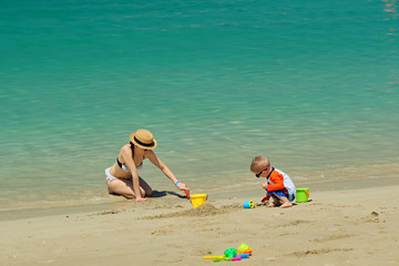 Two year old toddler playing with mother on beach
