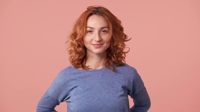 Portrait of european readhead woman 20s wearing basic shirt shaking her beautiful red hair, isolated over pink background in studio