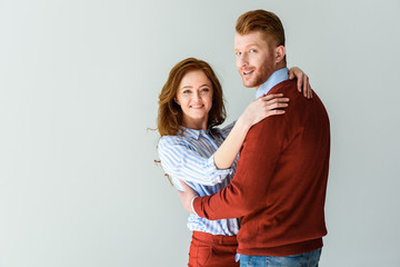 beautiful happy red haired couple hugging and smiling at camera isolated on grey