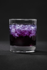 A one-color, purple clear cocktail in a low glass with crushed ice frappe. Side view. Isolated black background. Drink for the menu restaurant, bar, cafe