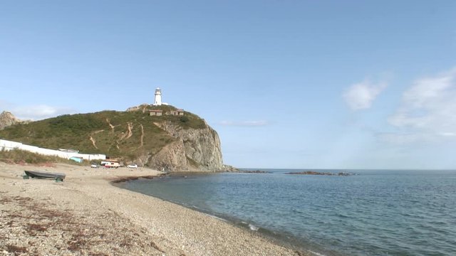 Lighthouse seamark on green stony rocks coastline beach in Japan Sea. Calmness and silence. Rest and tourism in beautiful place. Unique landscape and background.