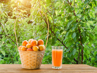Apricots in a wicker basket and a glass of juice on a green background, sunlight