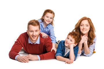 happy red haired family with two kids lying together and smiling at camera isolated on white