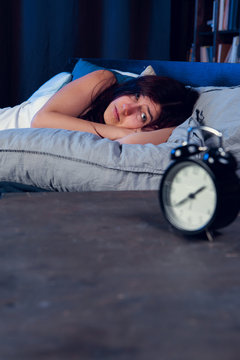 Photo of dissatisfied woman with insomnia lying on bed next to alarm clock at night