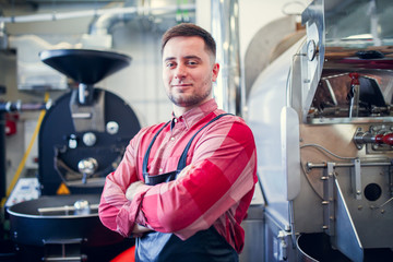 Image of young man in apron on background of industrial coffee grinder