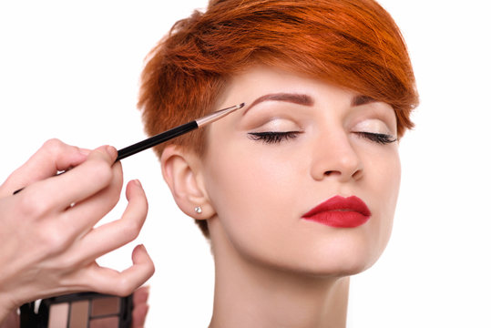 The artist is applying eyeshadow on her eyebrow with brush. The lady closed eyes with relaxation